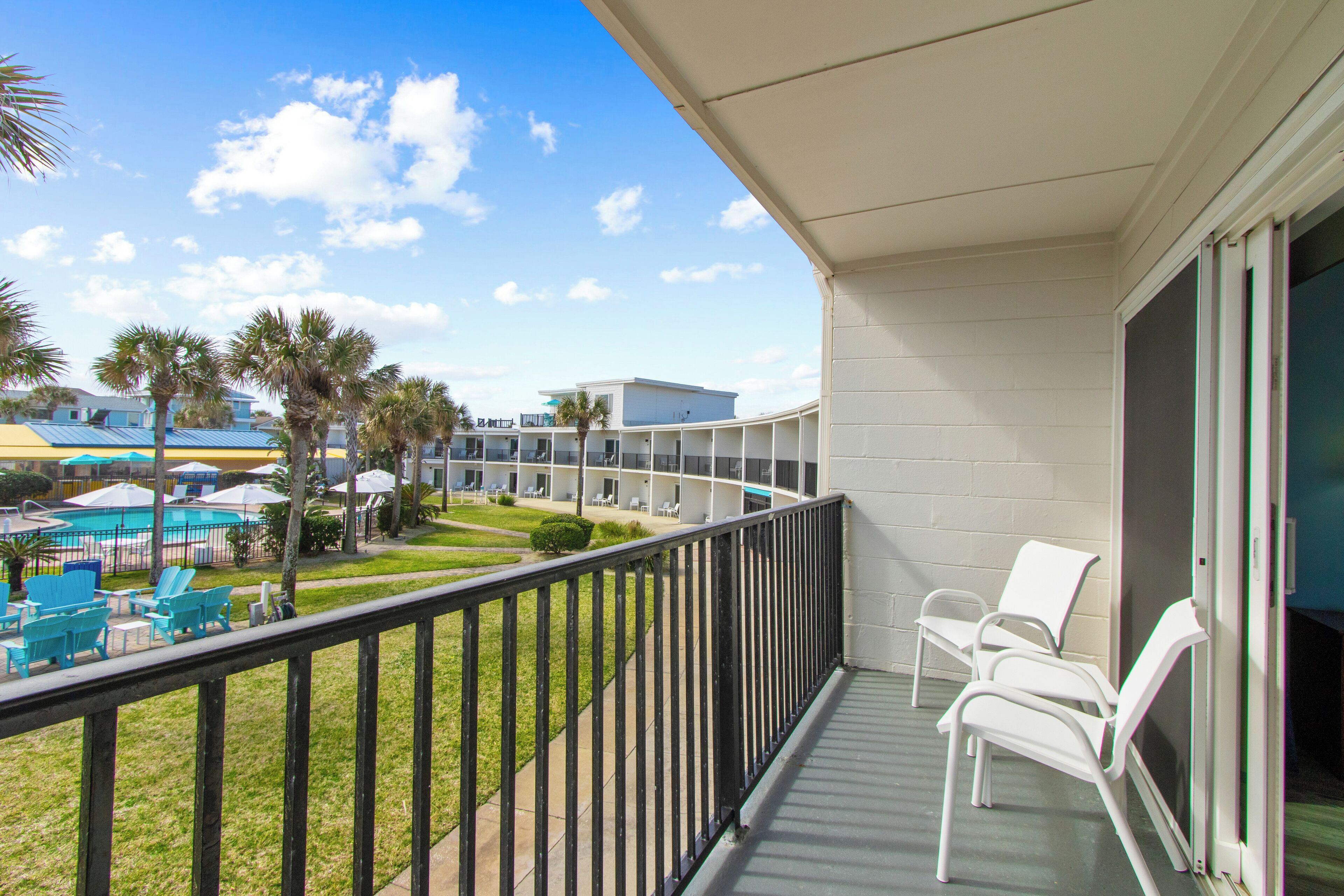 A balcony with white chairs, a pool, and a building with multiple floors and balconies.