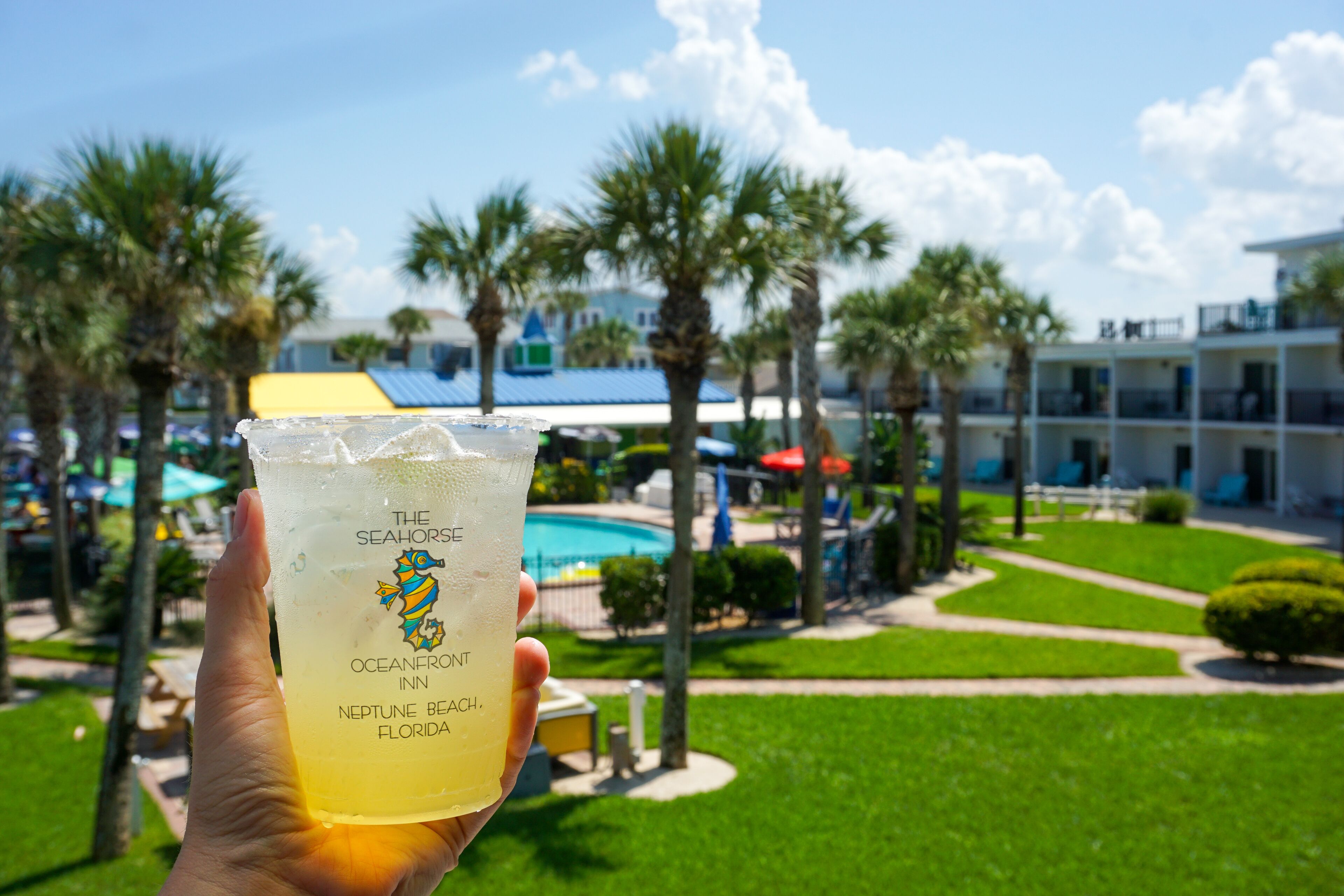 Una mano sosteniendo una bebida con una etiqueta que dice 'The Seahorses Oceanfront Inn Neptune Beach, Florida'.