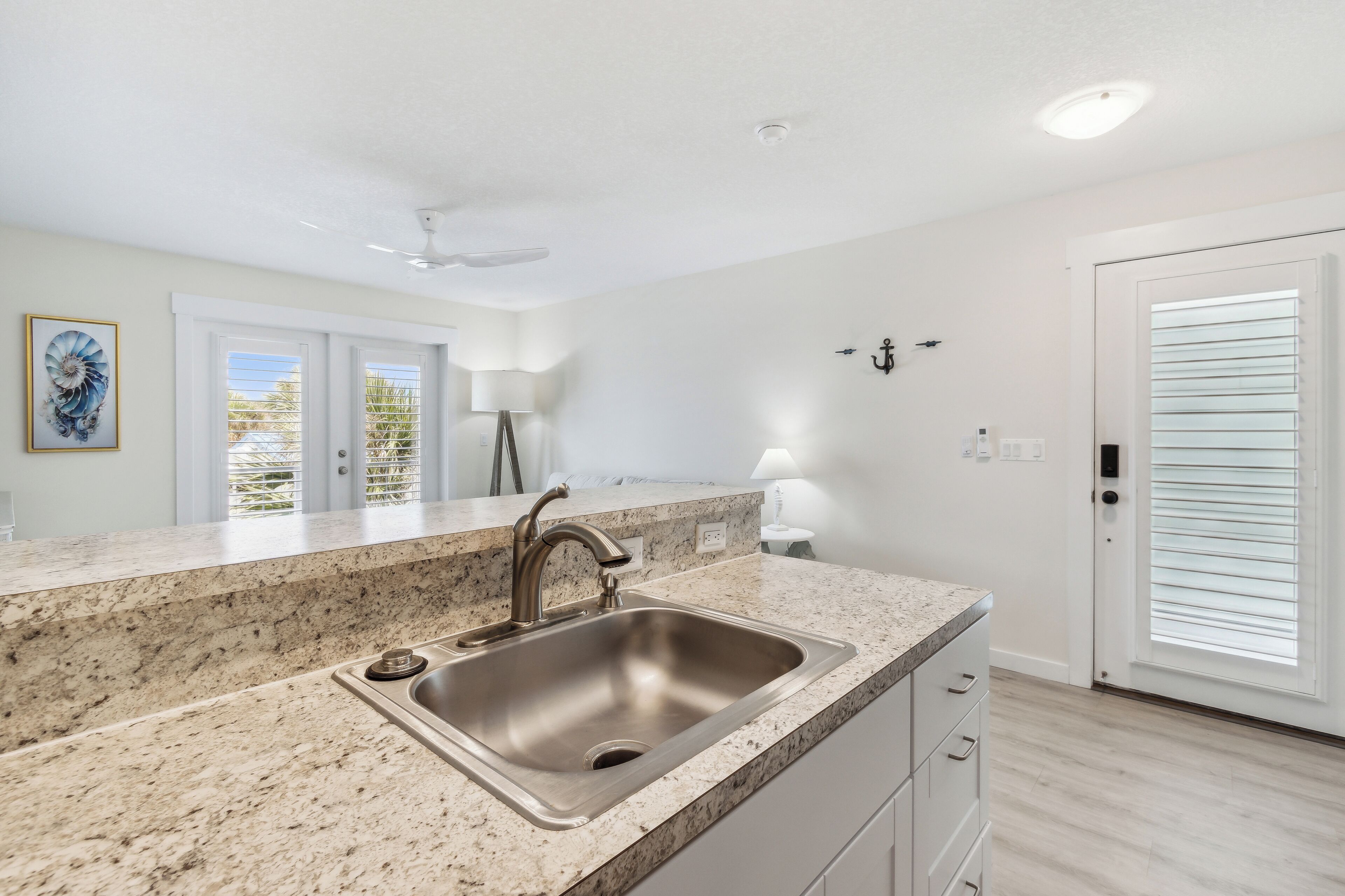 A kitchen with a granite countertop, stainless steel sink, and white cabinetry.