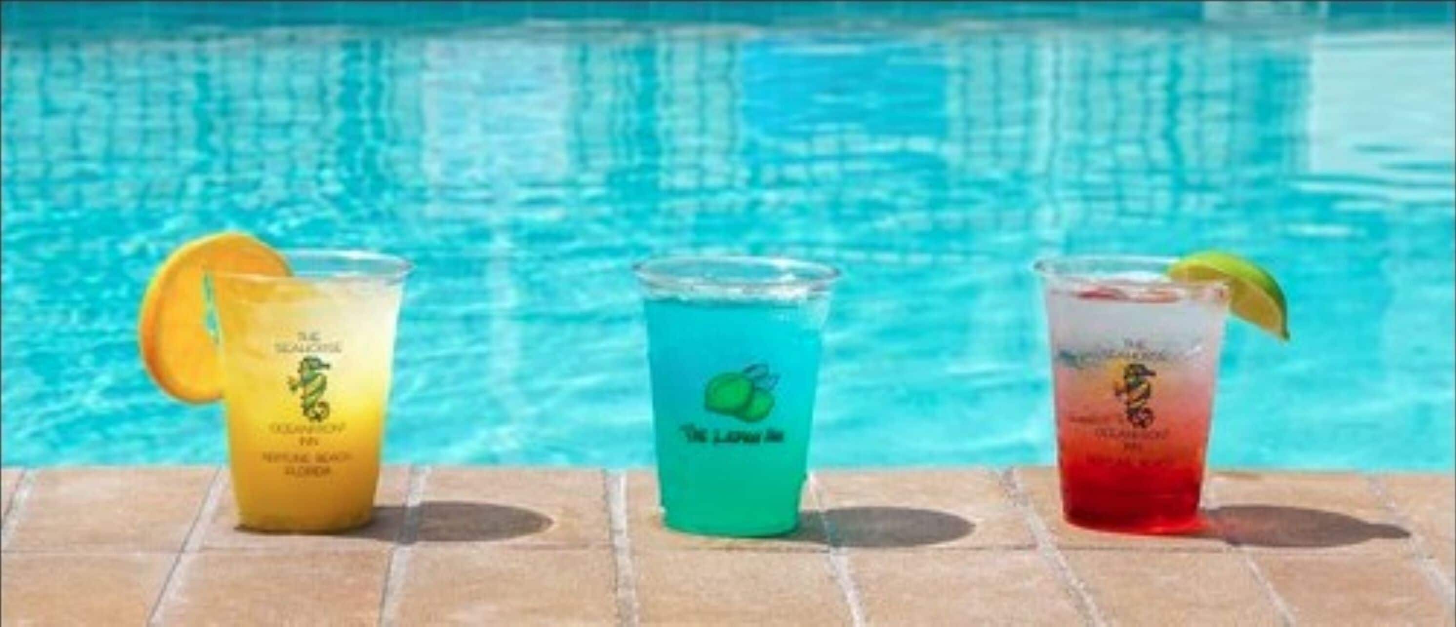 Trois boissons décorées de fruits, servies au bord d’une piscine.