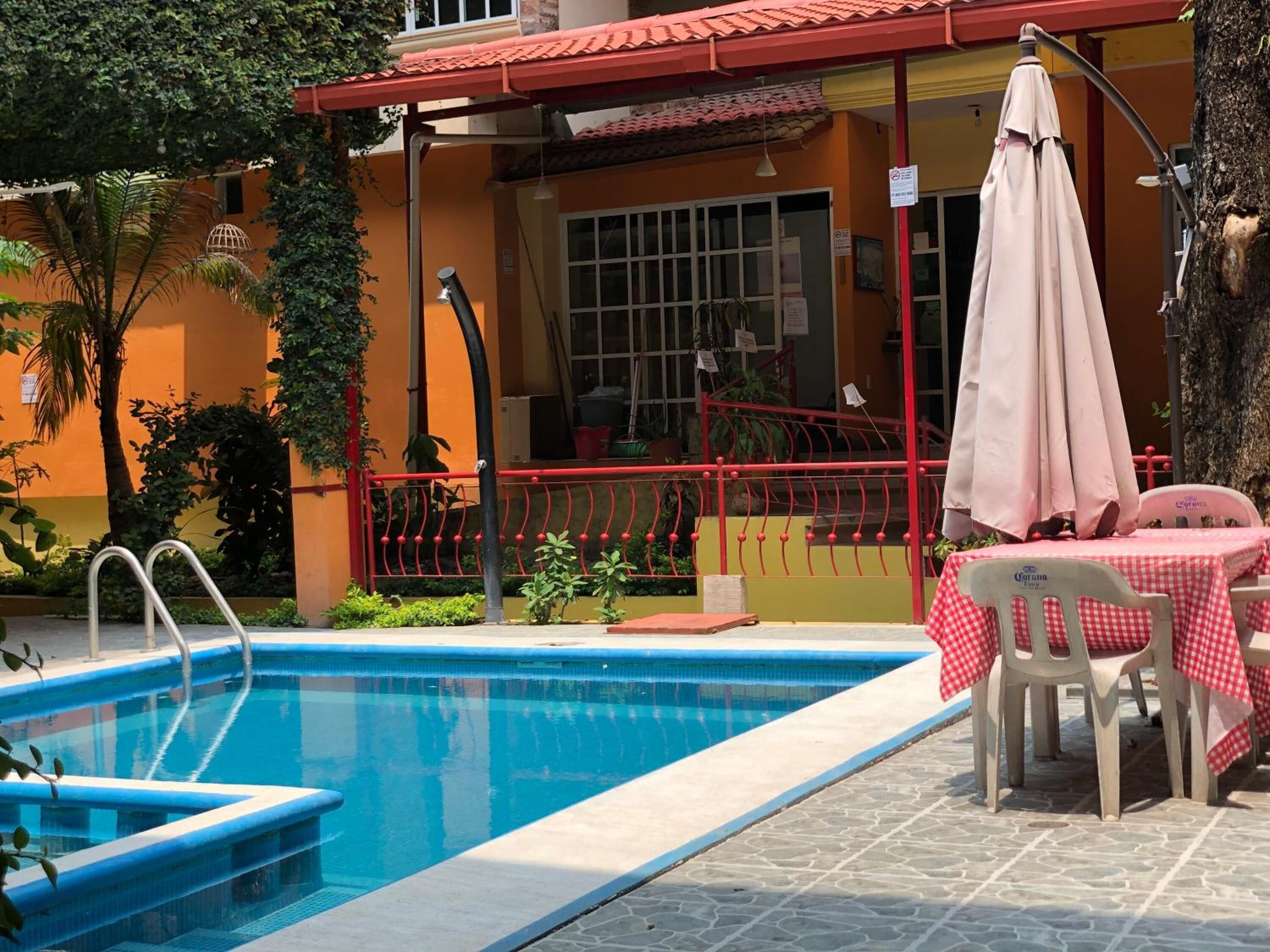 A swimming pool with steps, a red railing, and a table with a checkered tablecloth.