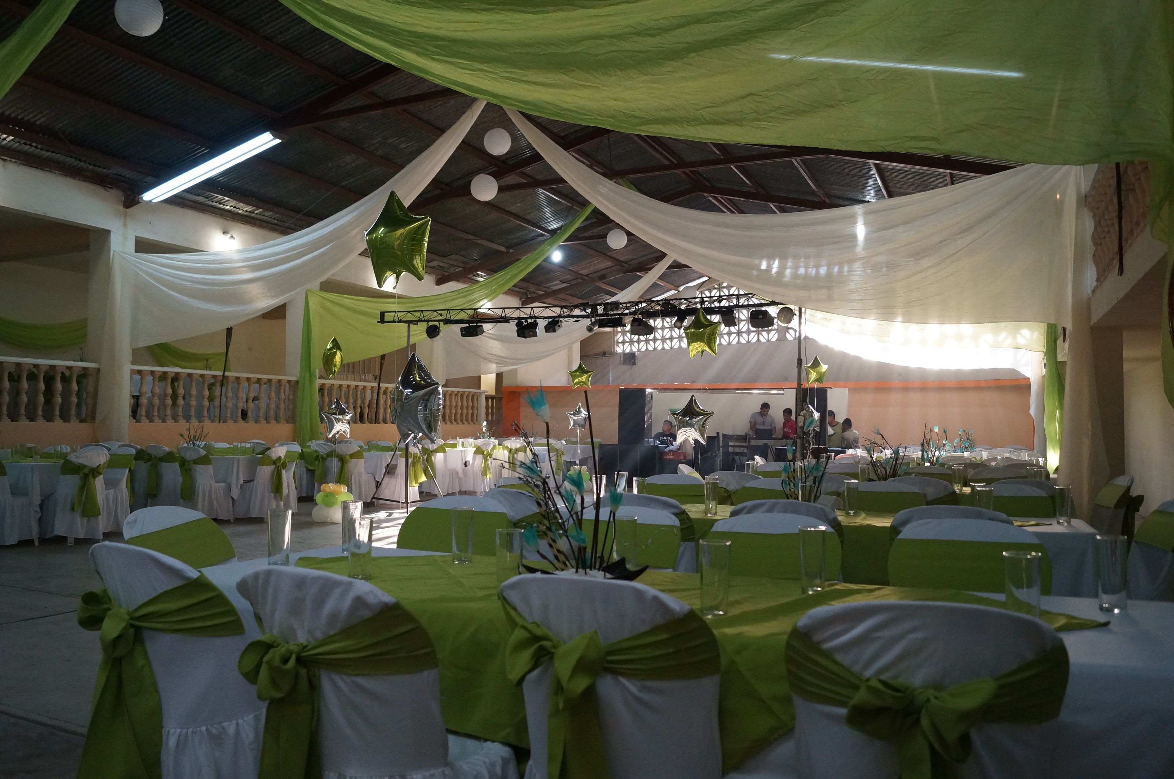 Un salón de banquetes con mesas dispuestas para un evento formal, cubierto con telas blancas y verdes y decoraciones en forma de estrella.