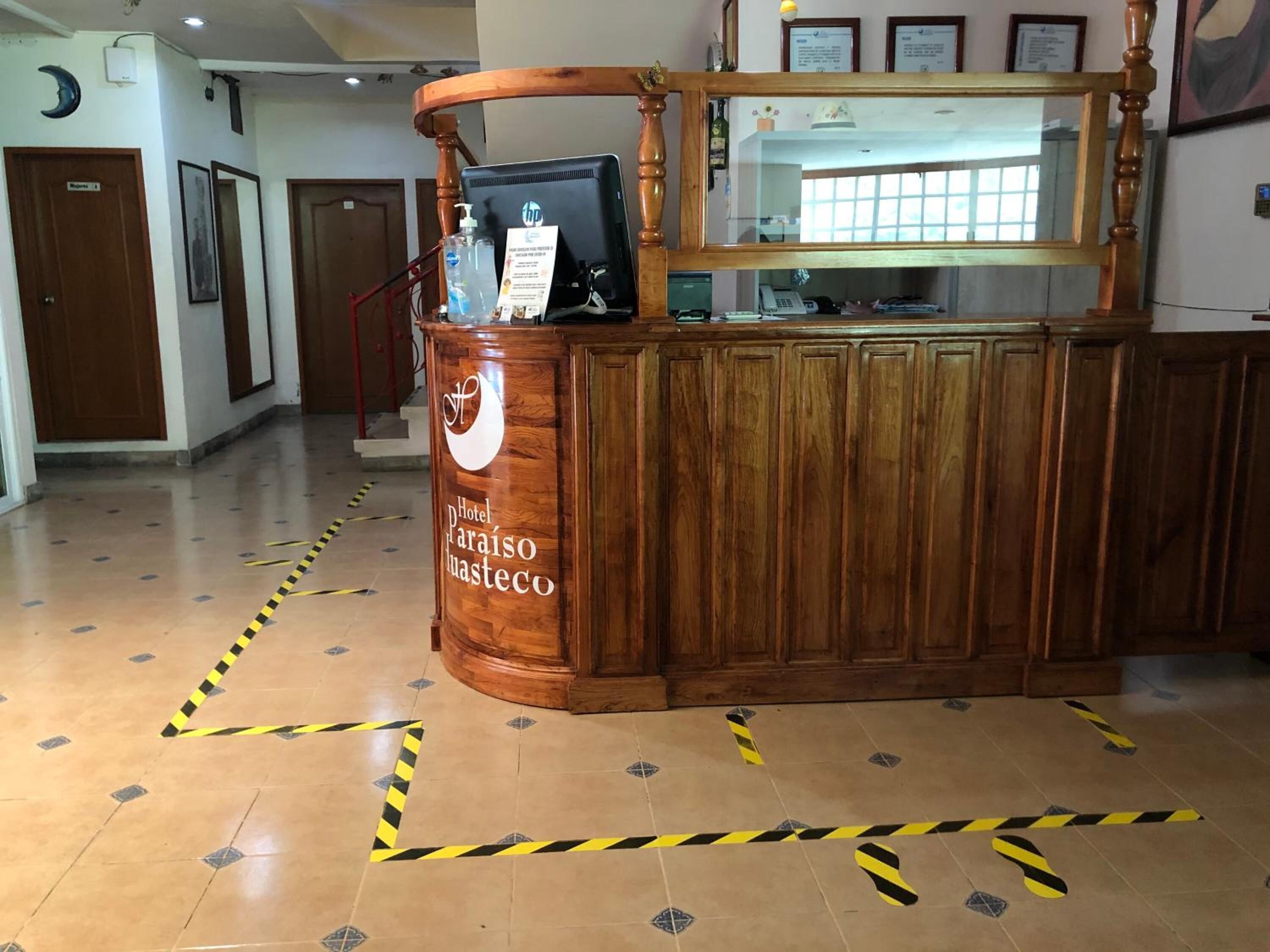 A reception desk with a wooden design, a computer monitor, and a sign indicating 'Hotel Paraiso Nasteco'.