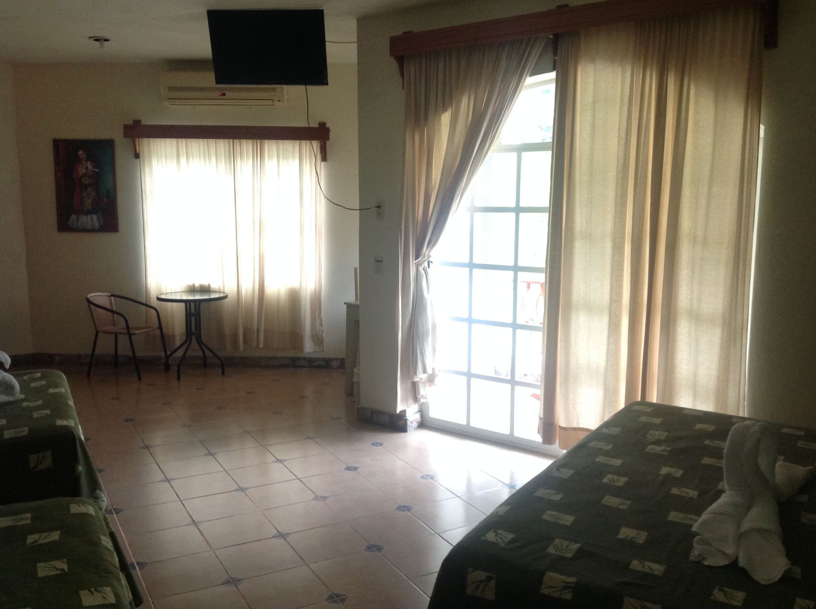 A hotel room with two beds, a small table, a chair, a TV, and a window with curtains.
