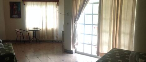 A hotel room with two beds, a small table, a chair, a TV, and a window with curtains.