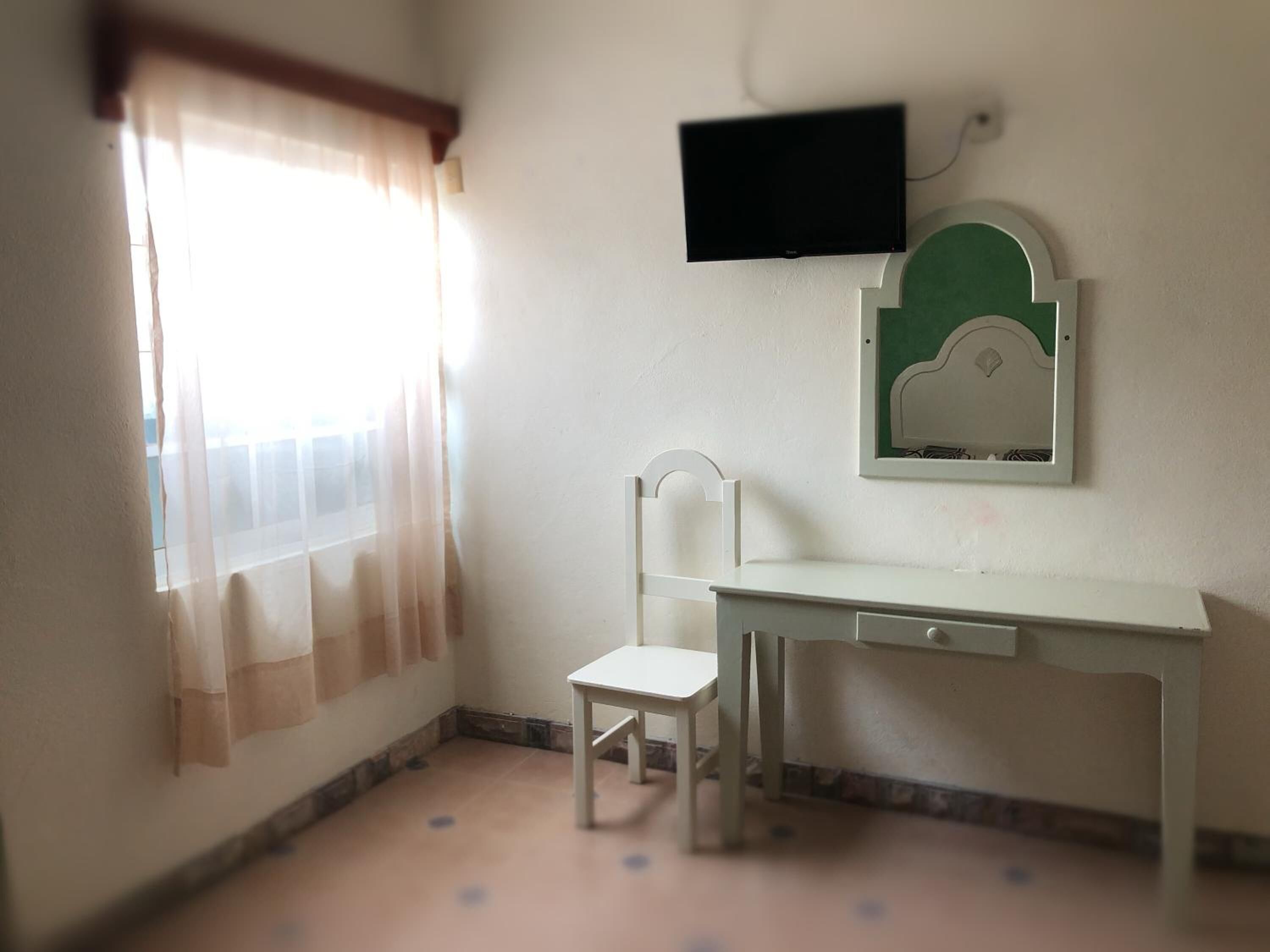 Une petite pièce simple, avec un bureau, une chaise et un téléviseur fixé au mur.