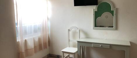 Une petite pièce simple, avec un bureau, une chaise et un téléviseur fixé au mur.