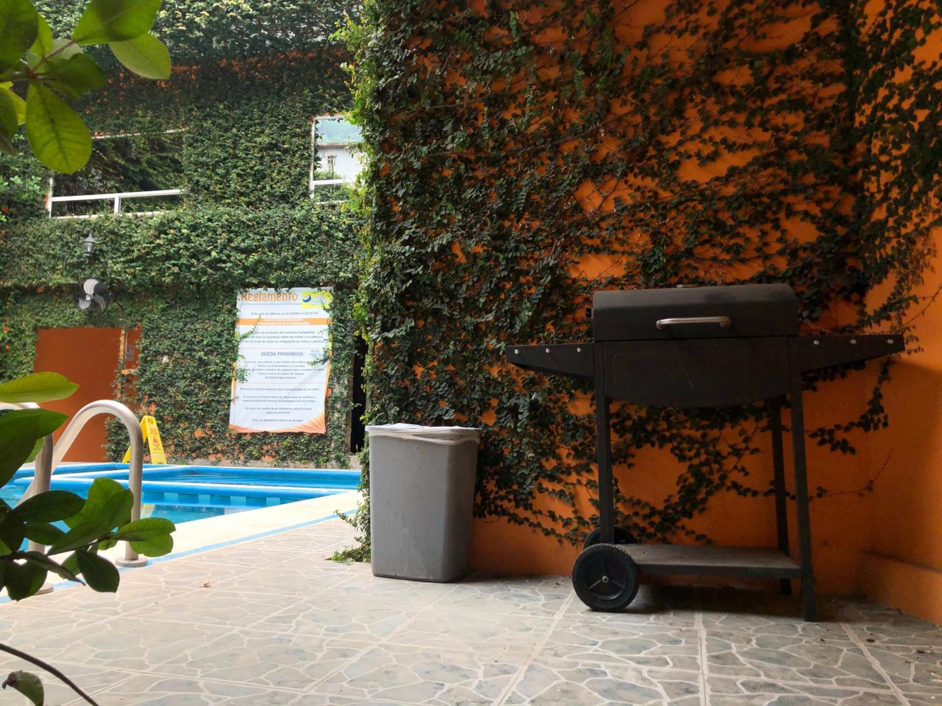 Un patio con una parrilla, un bote de basura y una piscina.