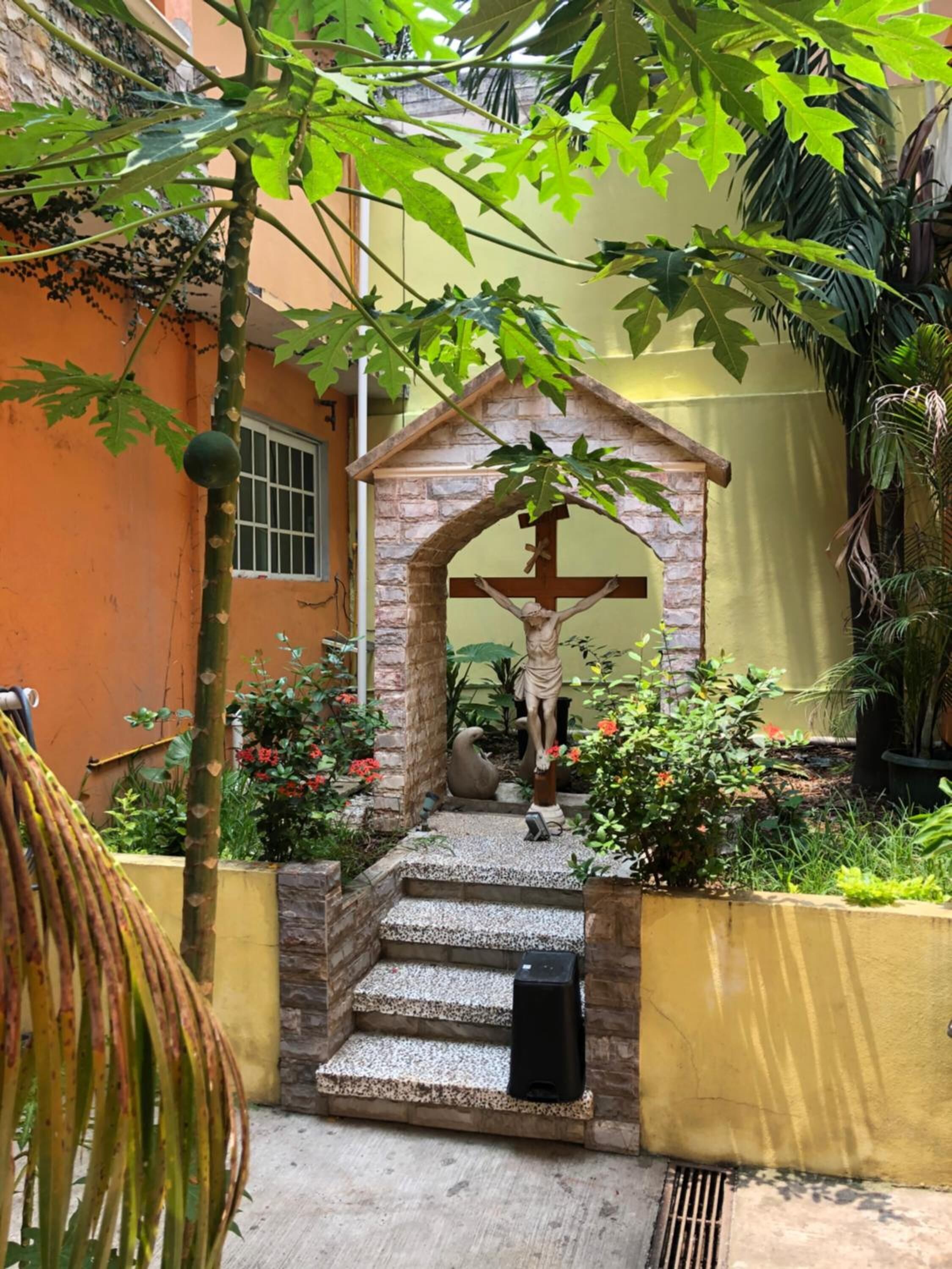 Um jardim com uma estátua de Jesus Cristo na cruz, cercado por plantas e flores.
