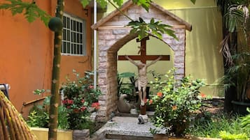 Um jardim com uma estátua de Jesus Cristo na cruz, cercado por plantas e flores.