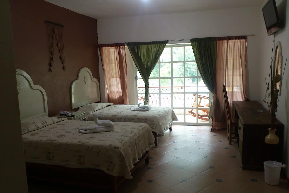 Una habitación con dos camas, un escritorio, una silla y un ventanal con cortinas.