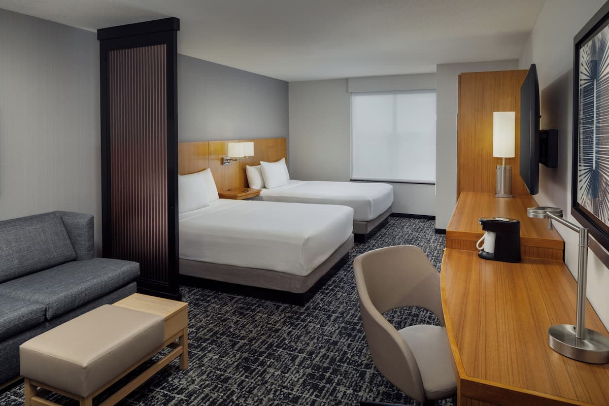 A hotel room with two beds, a sofa, a desk with a coffee maker, and a TV.