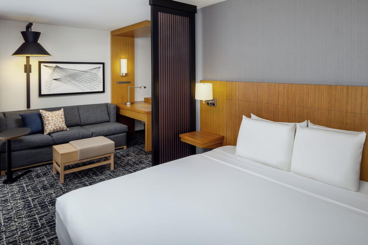 A hotel room with a bed, a sofa, a desk, and a lamp.