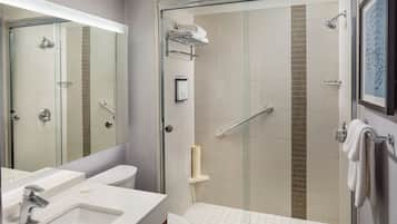 A modern bathroom with a glass-enclosed shower, a toilet, and a sink with a mirror above.