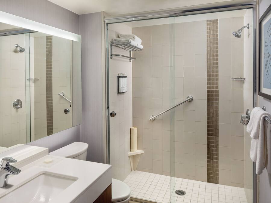A modern bathroom with a glass-enclosed shower, a toilet, and a sink with a mirror above.