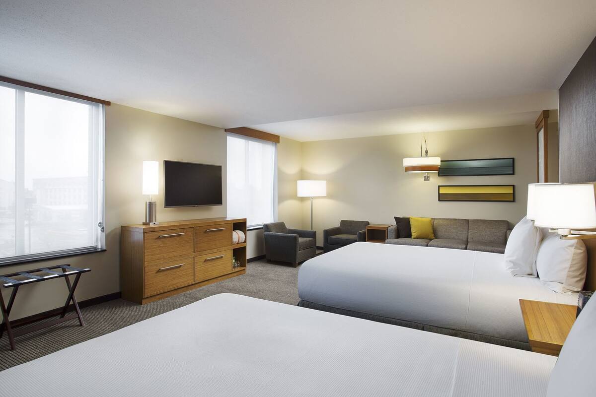 A hotel room with two beds, a TV, a desk, a chair, a lamp, and a window.