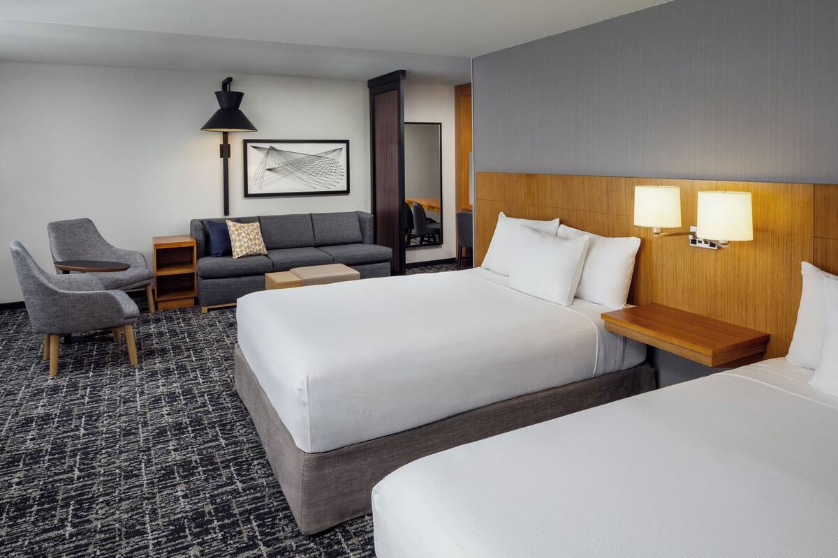 A hotel room with two beds, a sofa, a desk, and a chair.