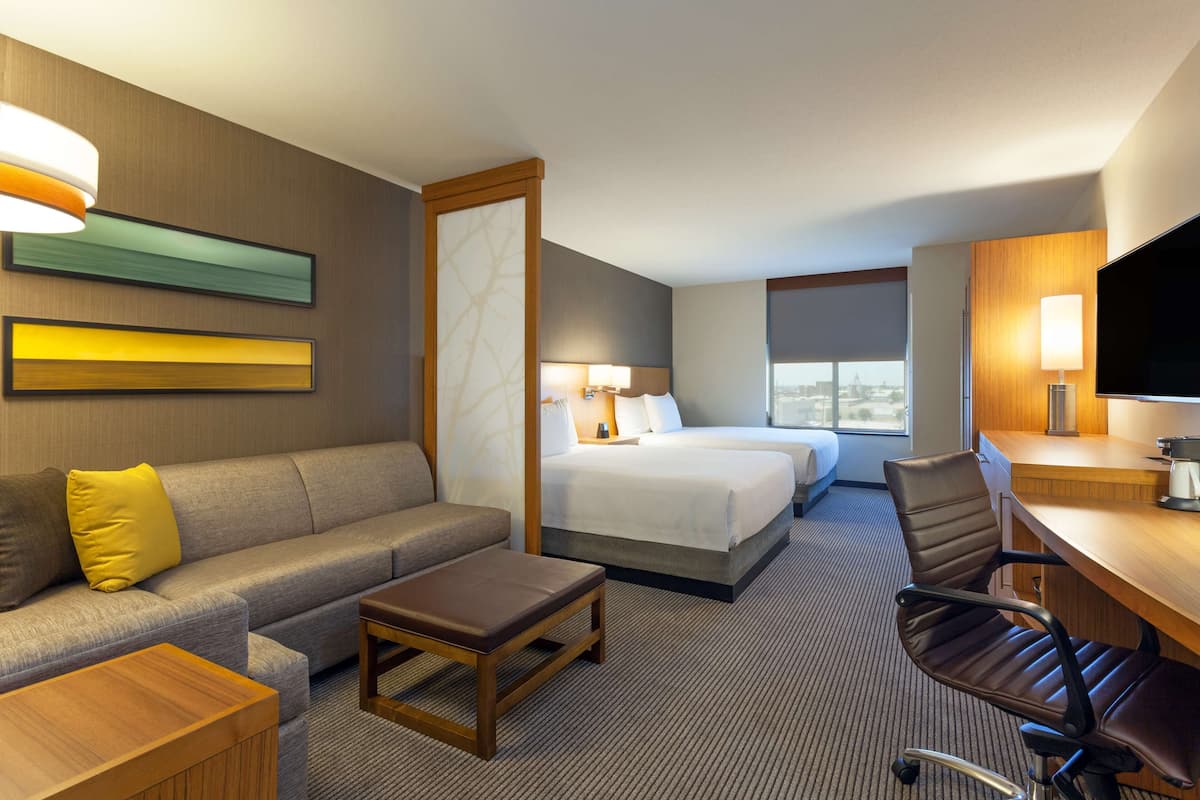 A hotel room with a sofa, a bed, a desk, a chair, and a TV.