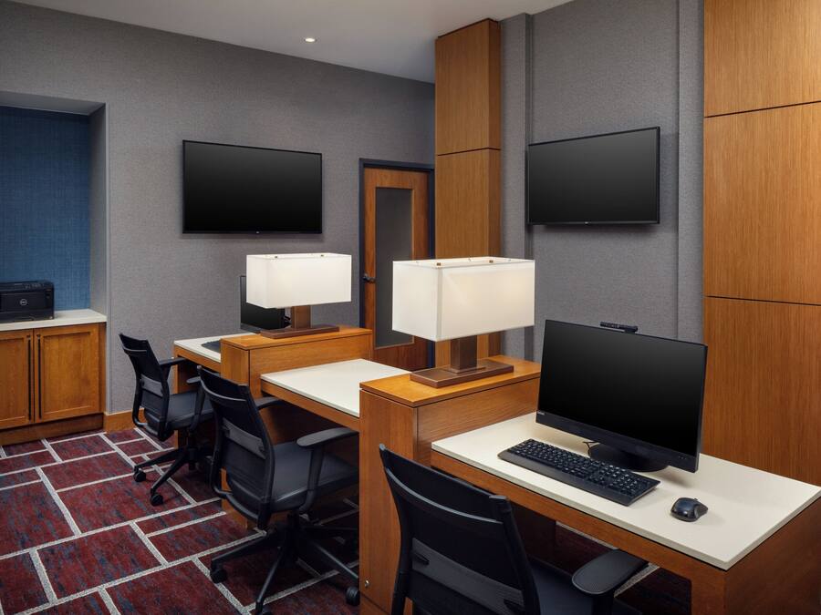 A hotel room with a desk, two chairs, a computer, two lamps, a television, and a wardrobe.