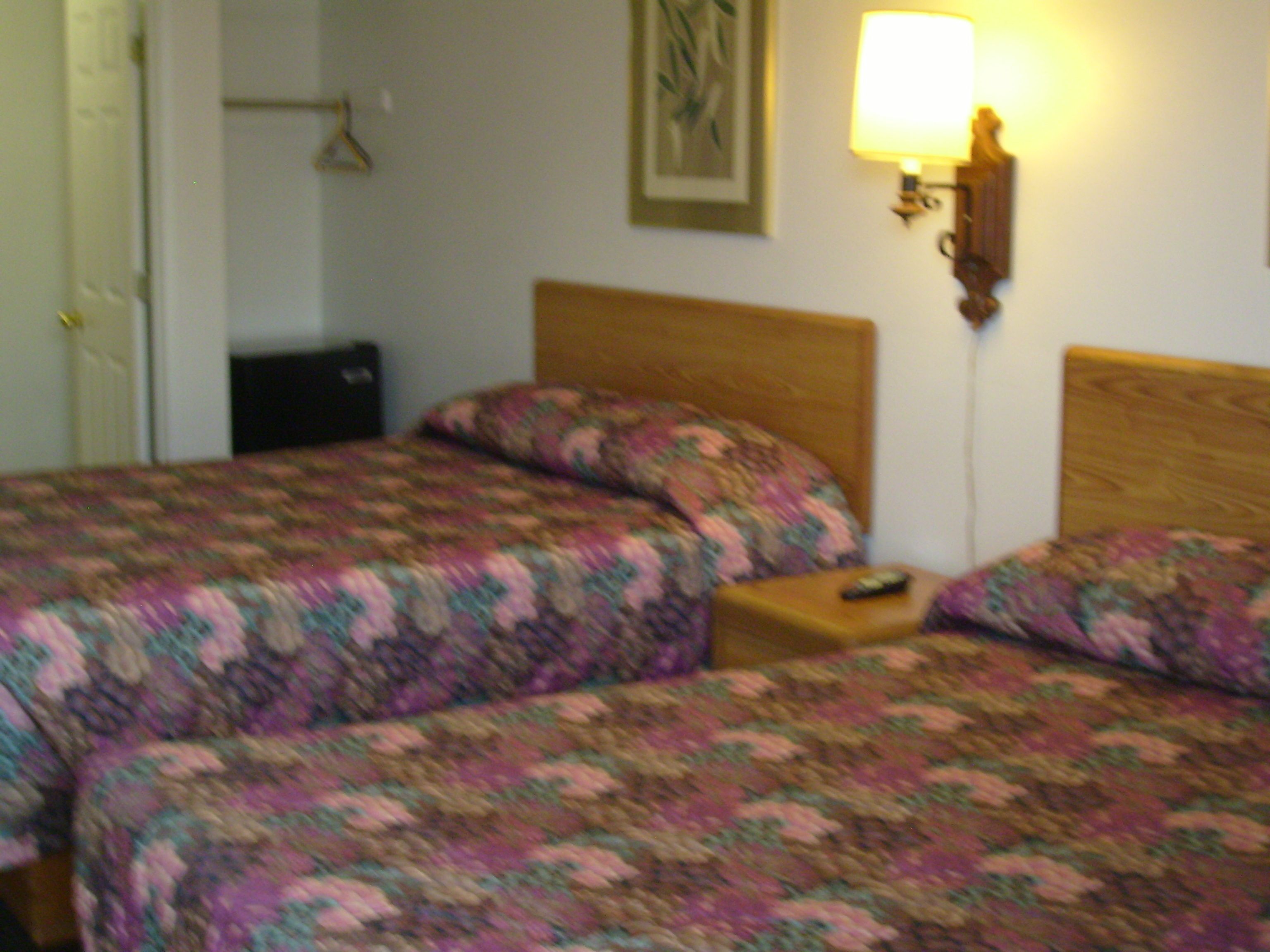 Una cama doble con cabecera de madera, una mesita de noche con control remoto y una lámpara fijada a la pared.