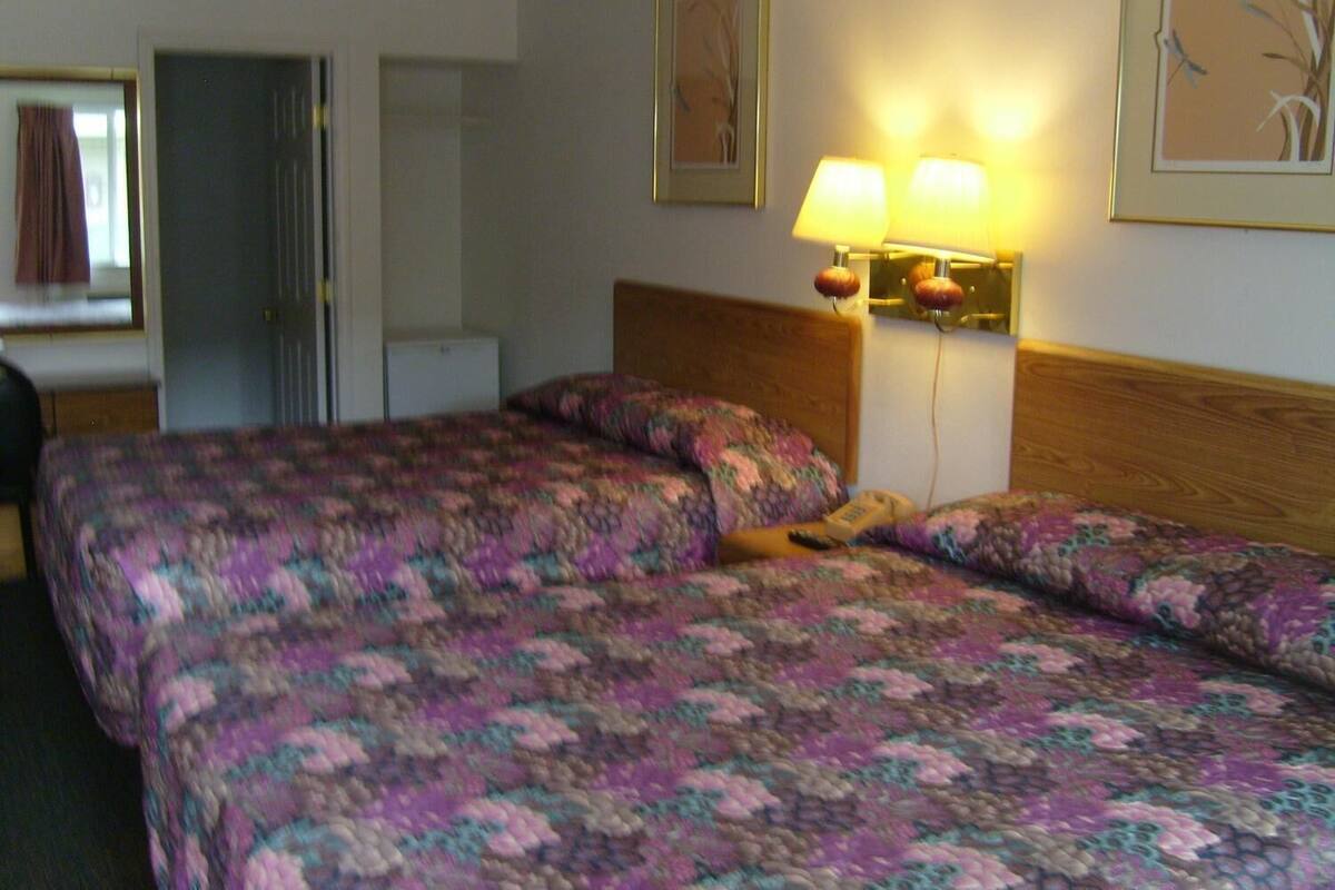 A hotel room with a bed, a desk, and a chair. There are two lamps on the wall and a picture frame above the bed.