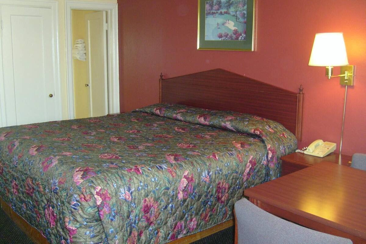 A hotel room with a bed, a nightstand, a lamp, and a painting on the wall.