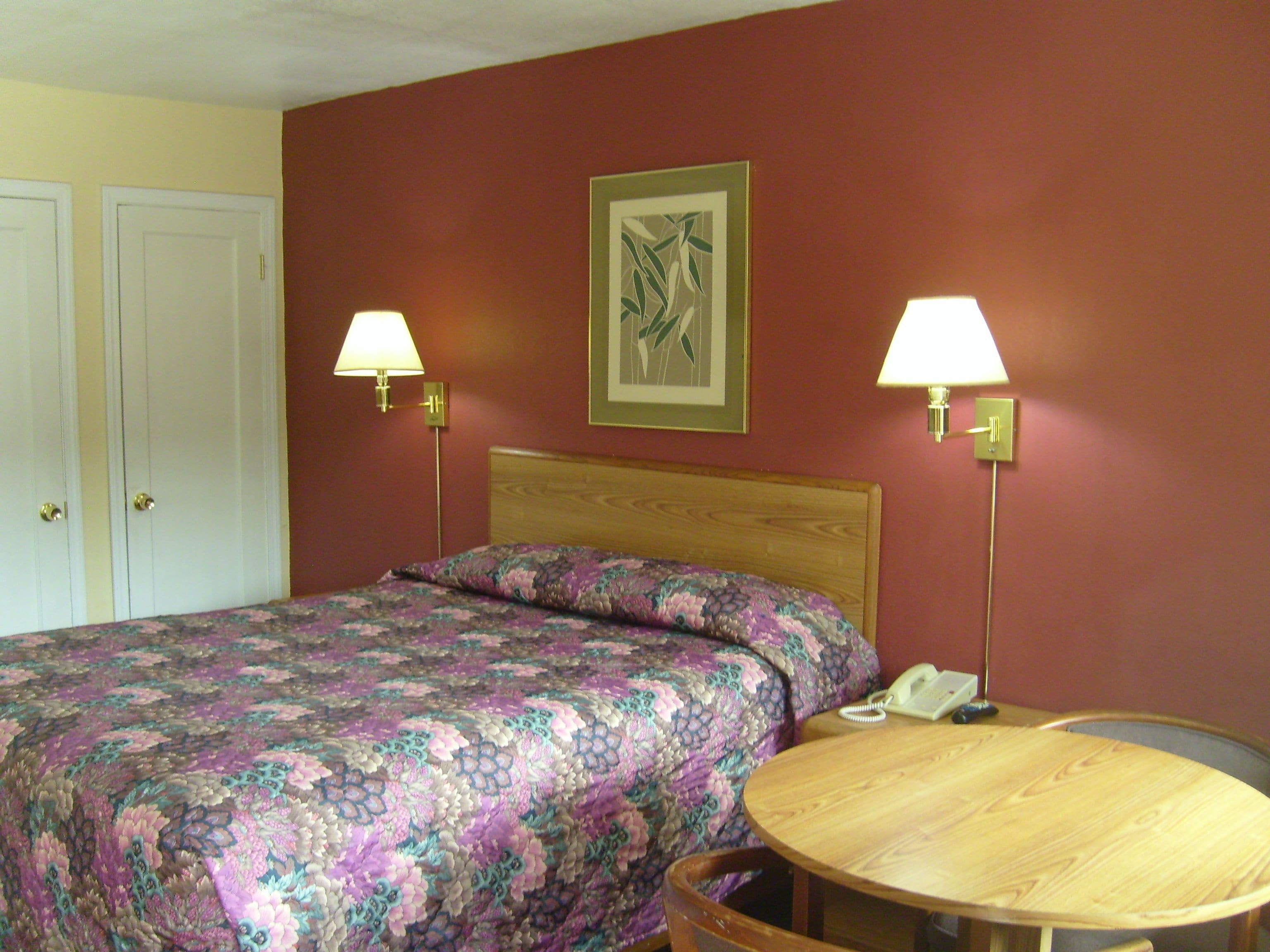 Habitación de hotel con una cama, dos lámparas de noche, una mesa redonda de madera y un teléfono.