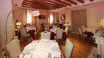 Comedor con varias mesas dispuestas para una comida, con manteles blancos y servilletas rojas.
