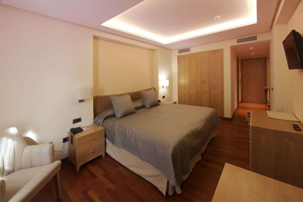 A modern bedroom with a large bed, bedside tables, a desk, and a TV.