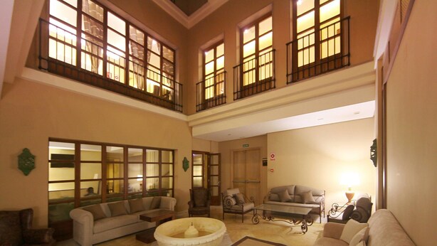 A spacious living area with multiple seating options, including sofas and armchairs, arranged around a central coffee table. Large windows with black railings provide natural light and views. - Hotel Casa Consistorial (Fuengirola)