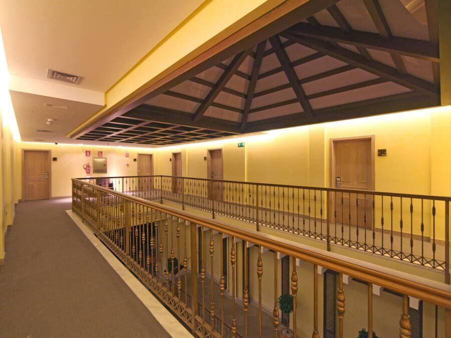 A hotel corridor with a wooden railing, a high ceiling with a truss structure, and doors leading to rooms.