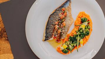 A white plate with a fish and vegetables on a dark mat.