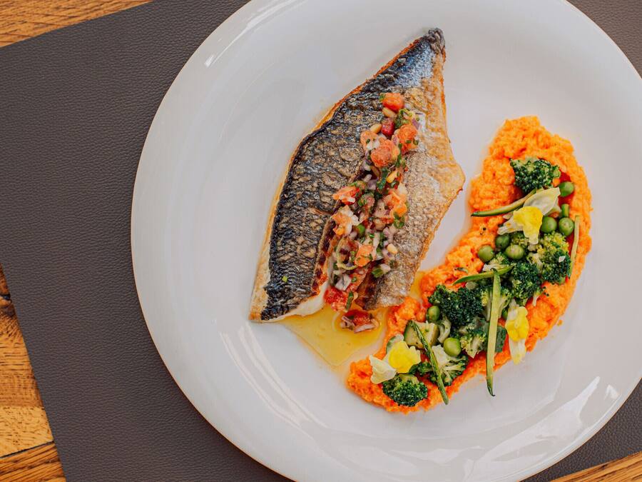 A white plate with a fish and vegetables on a dark mat.