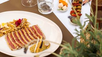 Una mesa de comedor con un plato de comida, una copa de vino blanco y un cuenco pequeño de aceitunas.