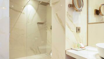 Un baño moderno con ducha envuelta en vidrio, paredes de mármol y un tocador con artículos de aseo.
