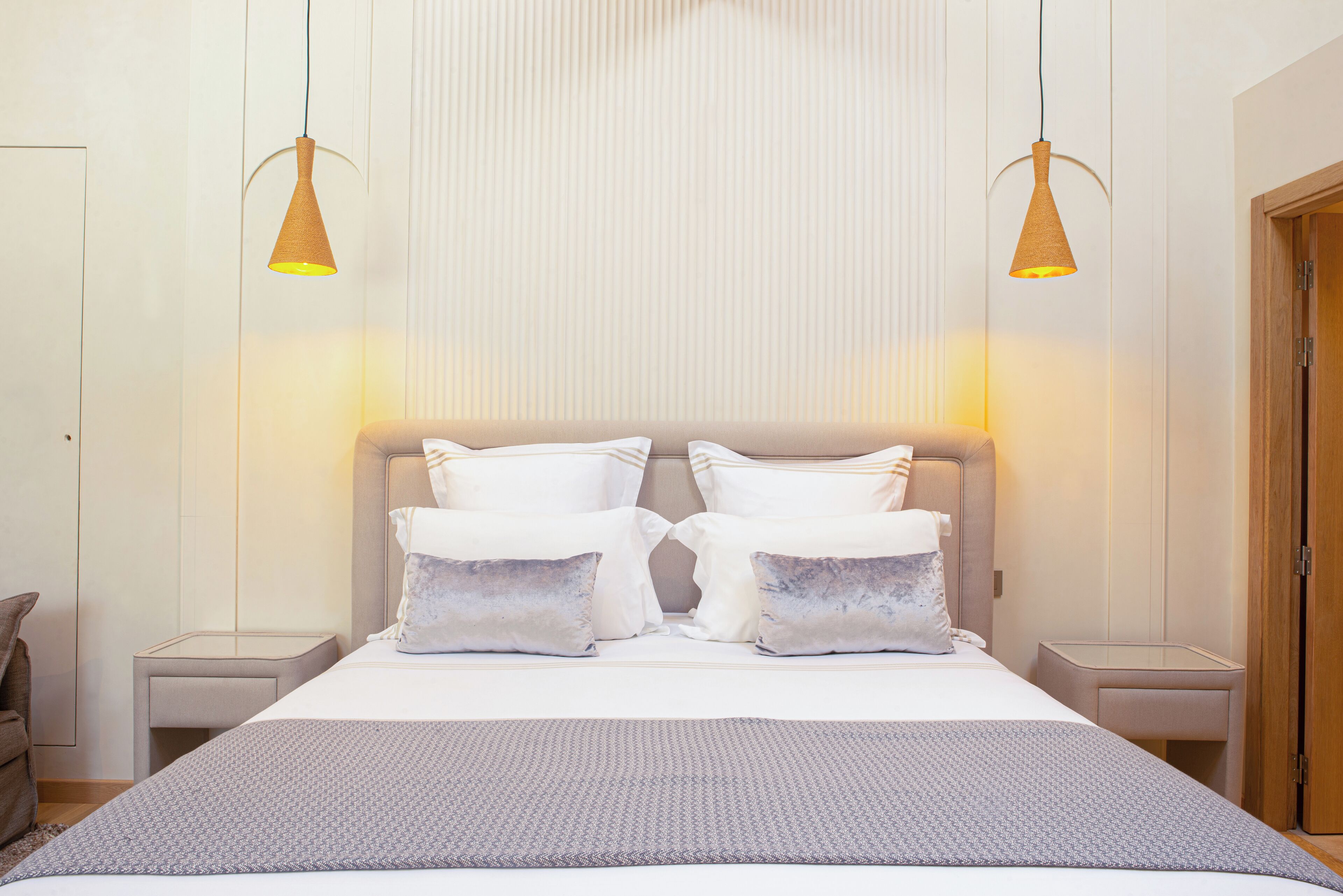 Une chambre d’hôtel bien aménagée, avec un grand lit, deux tables de chevet et deux lampes suspendues.