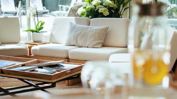 Een moderne woonkamer met een bank, een salontafel en een groot raam met uitzicht op tuinmeubilair en groen.