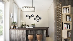 Een moderne keuken met een houten kookeiland, twee krukken, een hanglamp en een boekenkast.
