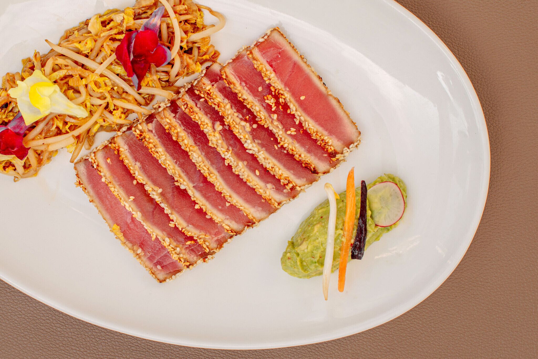 A plate with sliced tuna, noodles, and a small salad.