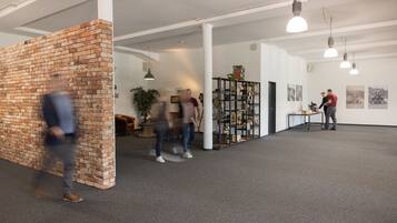 An interior space with exposed brick walls, a central column, and a ceiling with track lighting. There are shelves with various items and a table with objects on it.