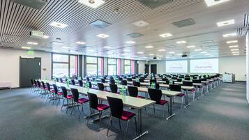A conference room with long tables, chairs, and a projector screen.