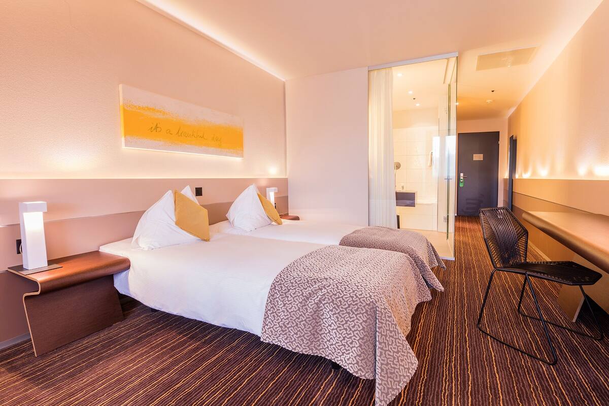 Una habitación de hotel con una cama grande, mesitas de noche, una silla y un espejo.