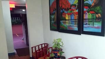 A hallway with patterned flooring, red chairs, a small table with a plant, and two paintings on the wall.