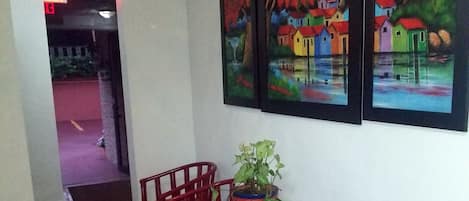 Un couloir avec un revêtement de sol à motifs, des chaises rouges, une petite table avec une plante et deux tableaux accrochés au mur.