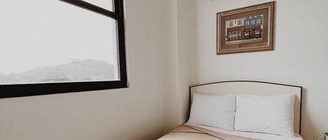 Une chambre d’hôtel avec un lit, une fenêtre, un appareil de climatisation et un tableau encadré au mur.