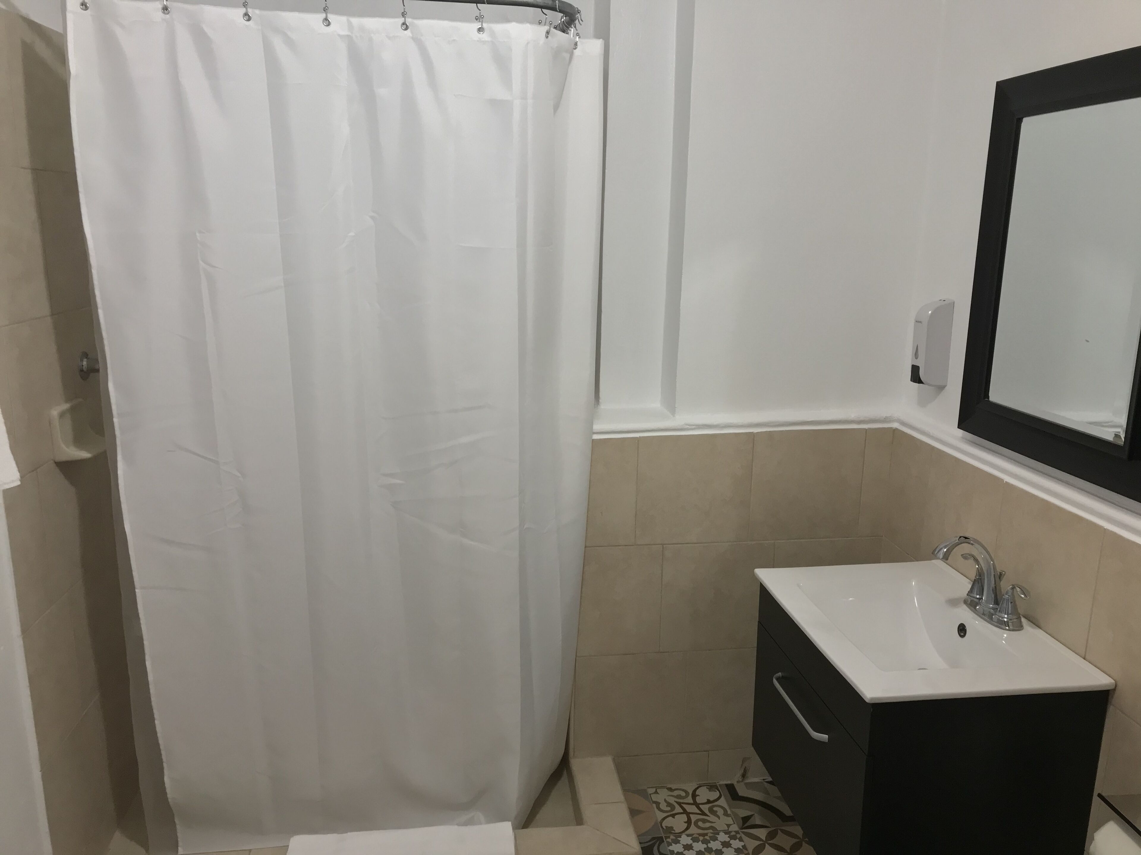 Un baño con cortina de ducha blanca, lavabo con gabinete negro y espejo sobre el lavabo.