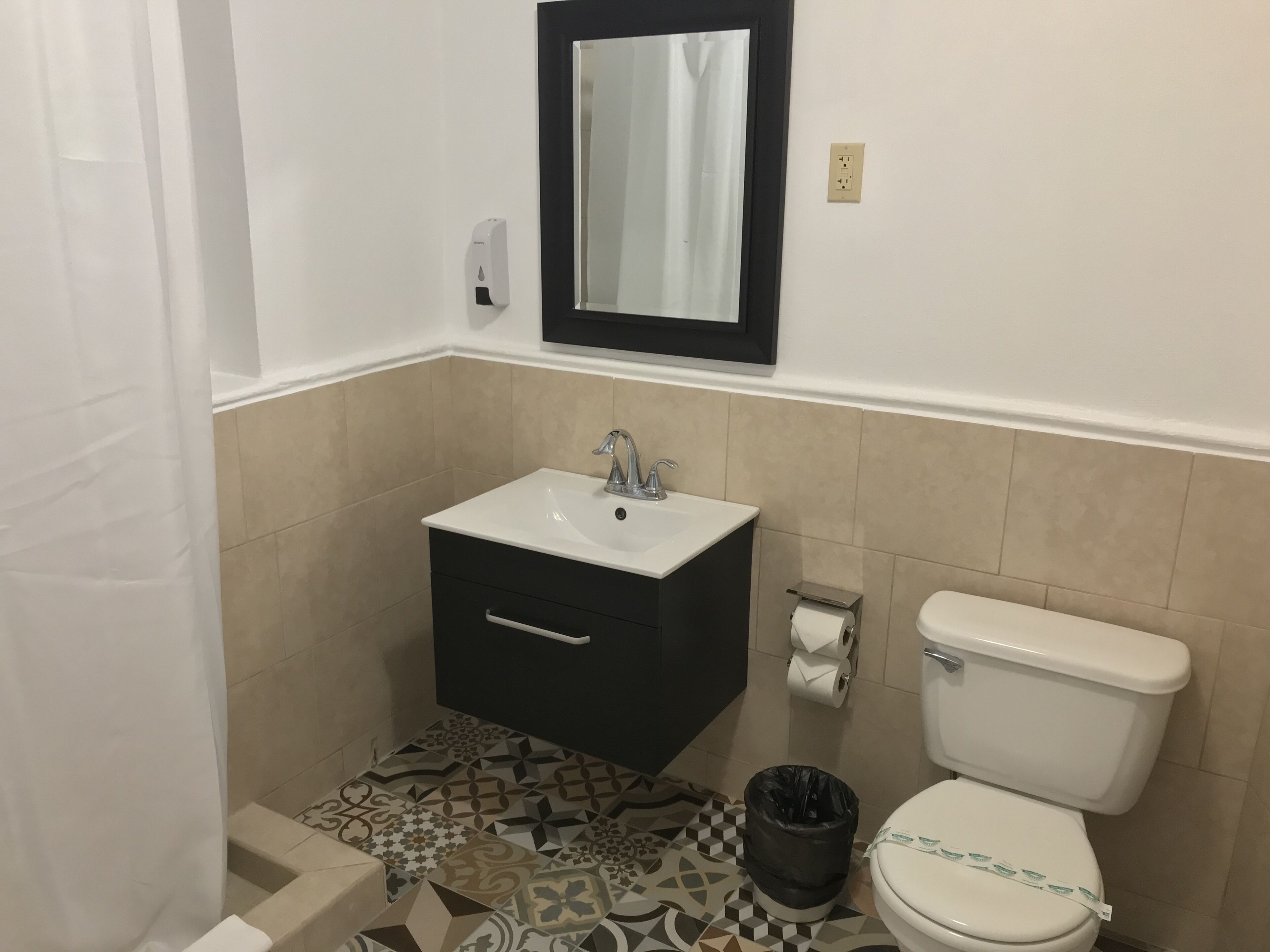 Un baño con lavabo, espejo, inodoro y baldosas de suelo estampadas.