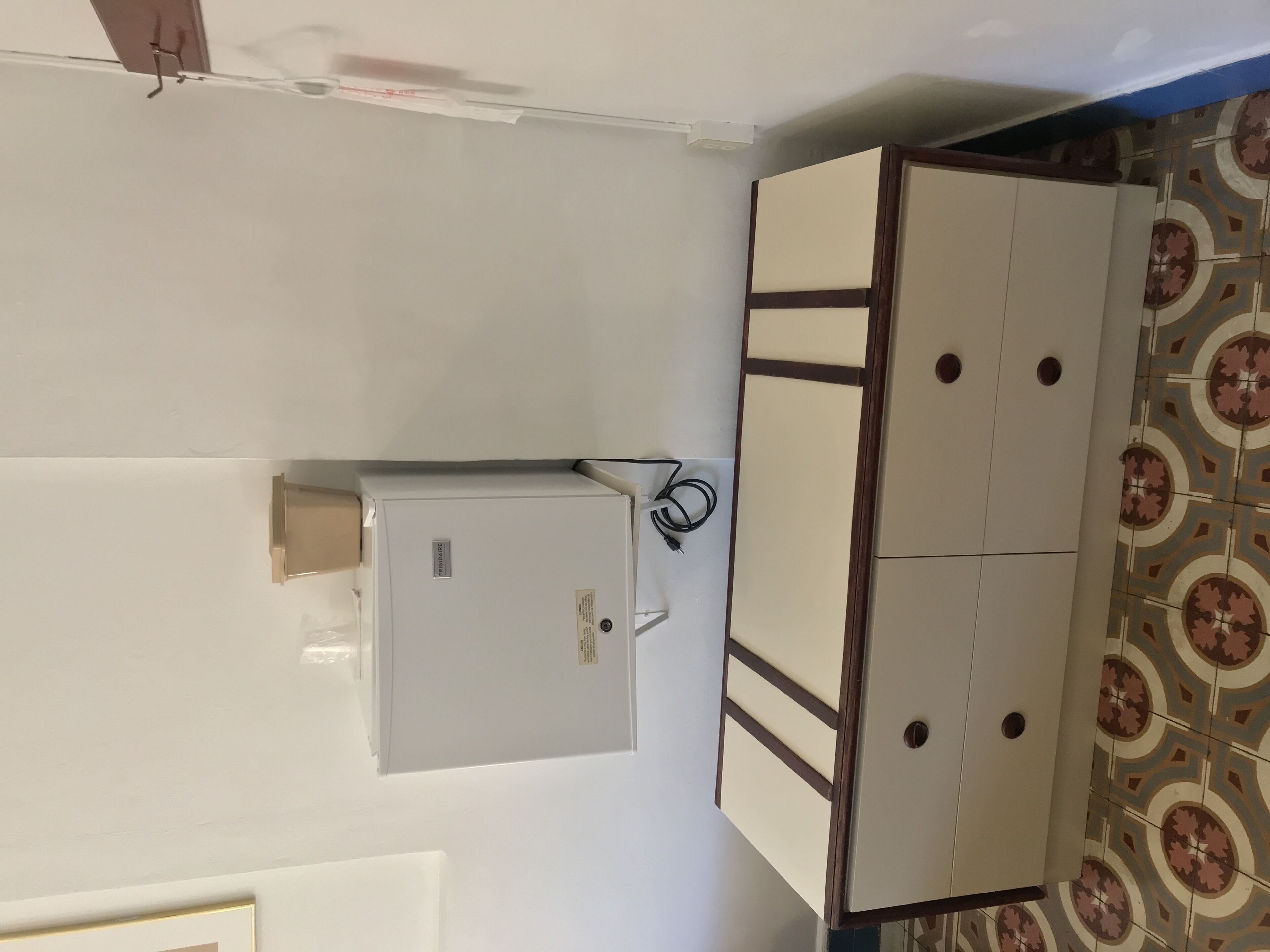 Una habitación con pared blanca, piso estampado y un mueble blanco con un cable enchufado.