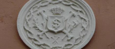 A circular emblem with a shield and crown, set against a plain wall.