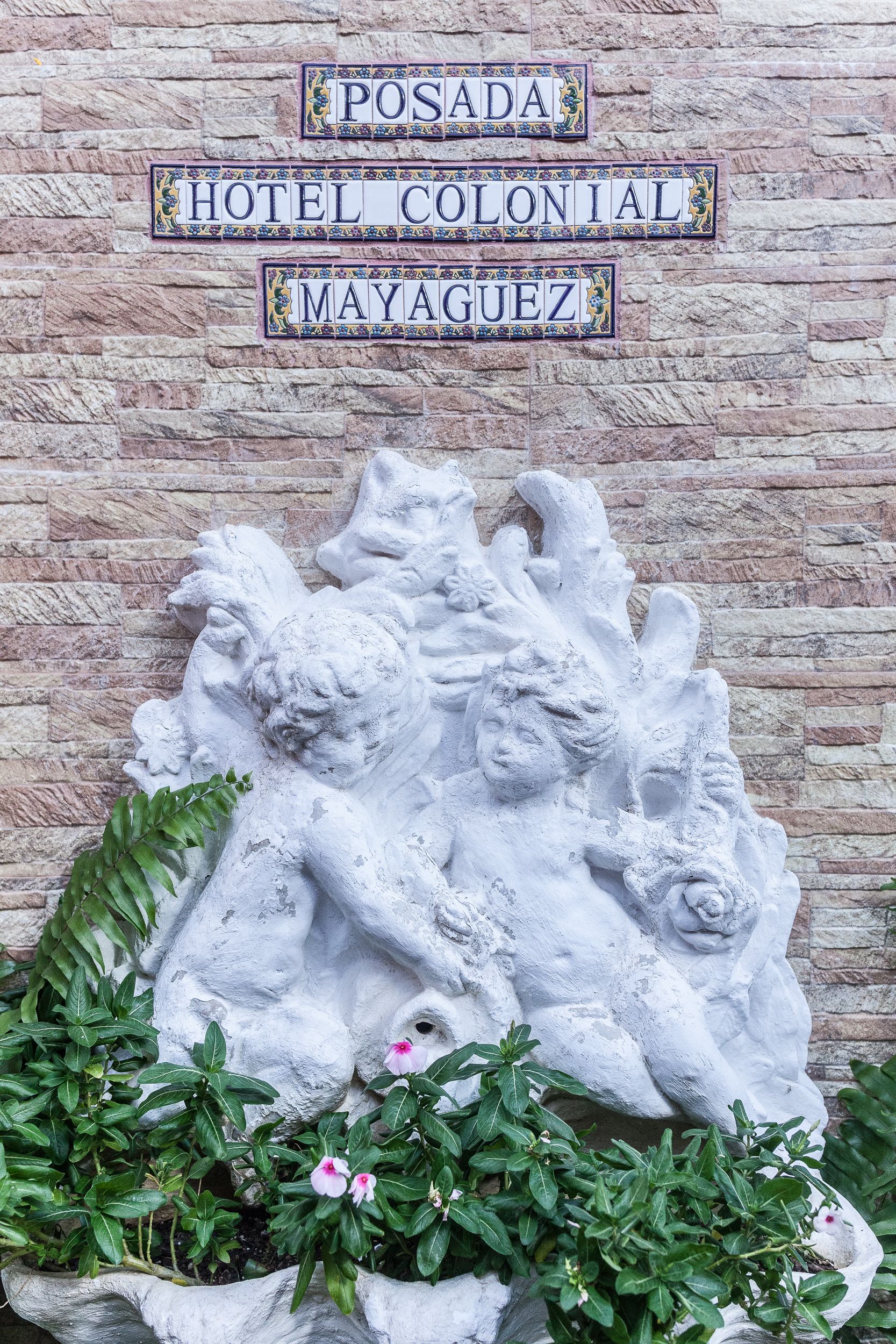 Eine Steinsäule mit dekorativer Reliefskulptur und einem Schild für 'Posada Hotel Colonial Mayaguez'.